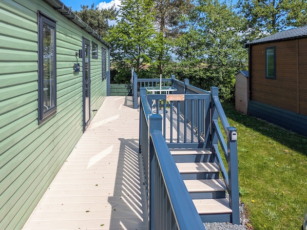 A wooden deck leading to a green building with a blue railing and a wooden bench.