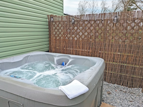Ein Whirlpool mit Handtuch, umgeben von einer Bambusumzäunung und einem grünen Gebäude.