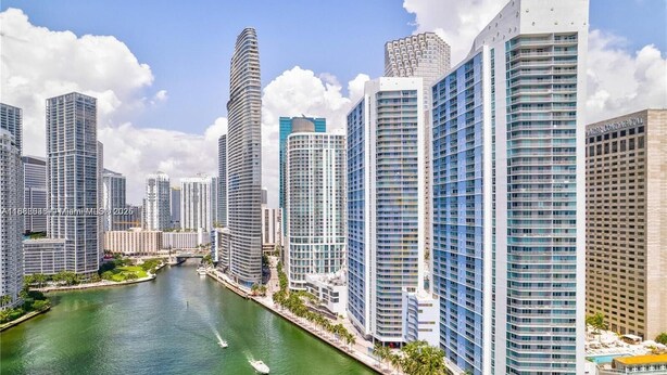Un quartier urbain dense, caractérisé par de nombreux immeubles de grande hauteur et traversé par une rivière, avec des bâtiments modernes et un port de plaisance où sont amarrés des bateaux.