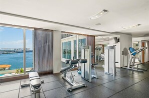 A modern gym with exercise equipment, large windows, and a view of the water.