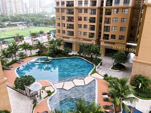 Un hotel con piscina, palme e vista su un campo sportivo.