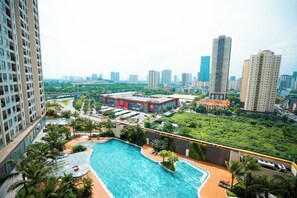 Un edificio alto con piscina sul tetto, circondato da vegetazione, un’area parcheggio e uno skyline sullo sfondo.