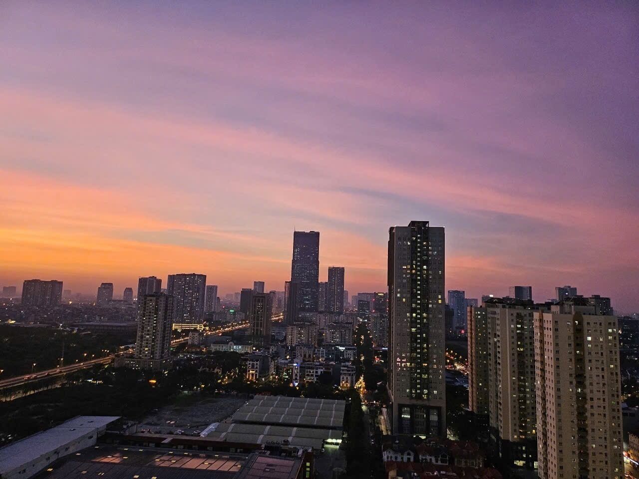 A cityscape at dusk with high-rise buildings and a highway.
