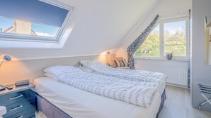 Een slaapkamer met twee bedden, een dakraam, een raam, een nachtkastje met een lamp en een radiator.