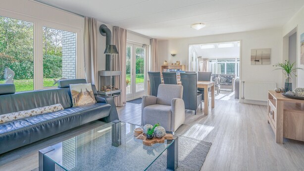 Een ruime woonkamer met een leren bank, een glazen salontafel en uitzicht op de tuin door grote ramen.