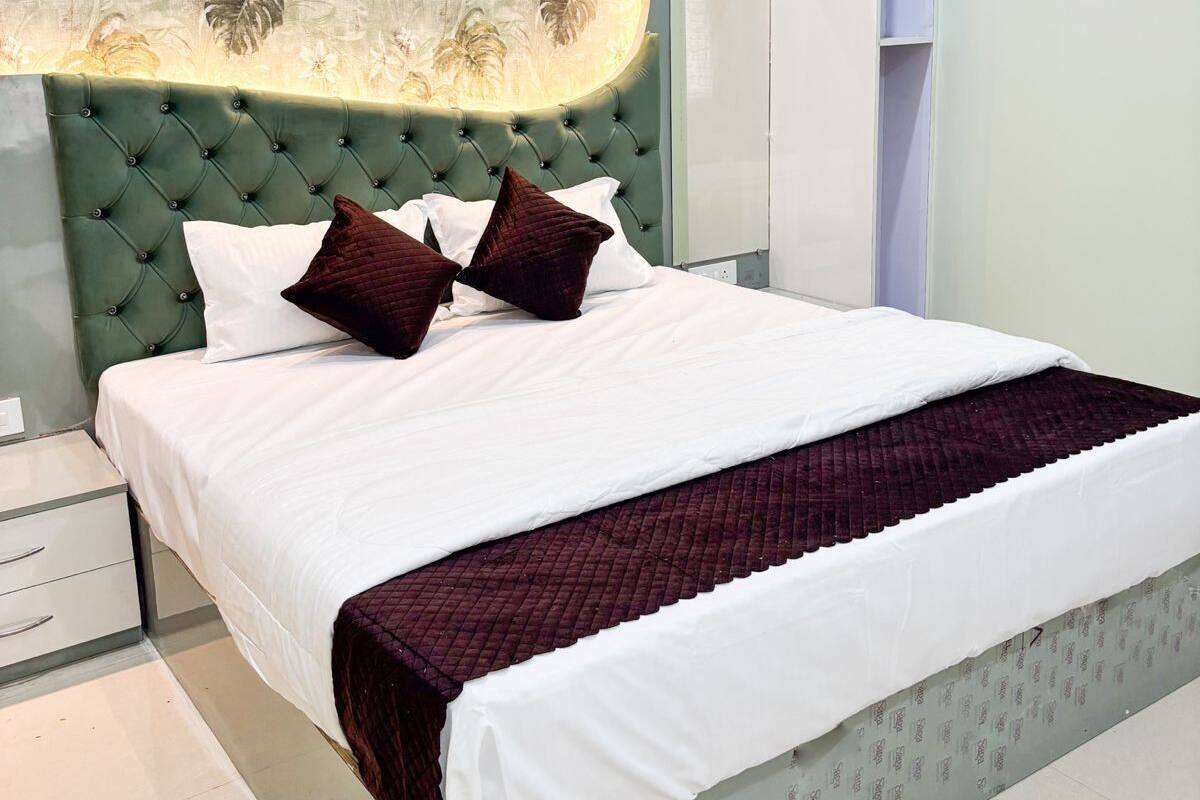 Un dormitorio moderno con un cabecero capitonado, una cama grande con ropa de cama blanca y rojo oscuro, y un panel decorativo sobre la cama.