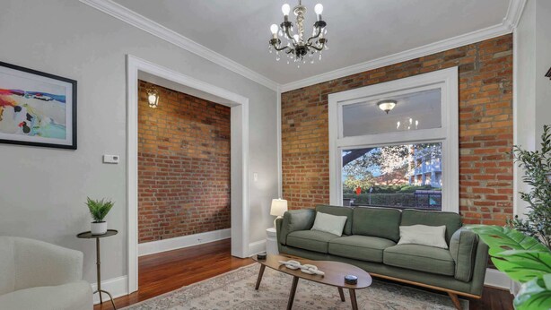 A living room with a green sofa, a coffee table, a patterned rug, a potted plant, and a brick wall.