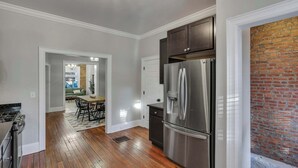 A kitchen with a stainless steel refrigerator, wooden flooring, and a brick accent wall.