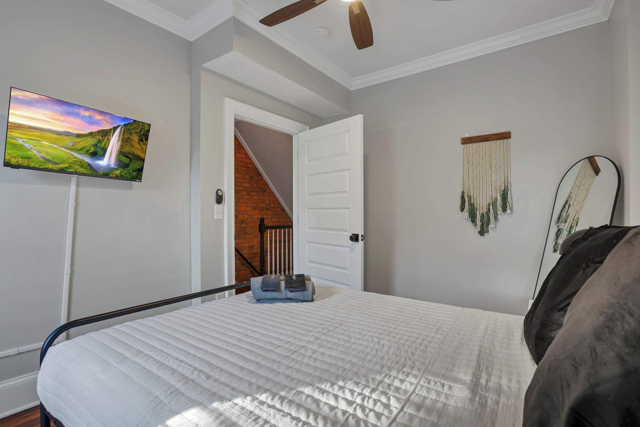 Une chambre à coucher comprenant un lit, un téléviseur fixé au mur, une porte donnant sur un escalier et une décoration murale.