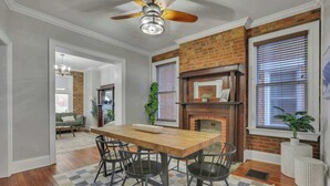 A dining area with a wooden table and chairs, a brick fireplace, and a ceiling fan.