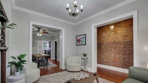 A living room with a brick wall, a chandelier, a dining area, and a white armchair.