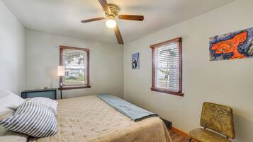 A bedroom with a bed, a chair, a ceiling fan, and two windows with blinds.