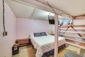 Une chambre avec un lit simple, un banc en bois, une petite poubelle et une structure de lit superposé.