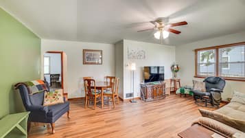 A living room with a wooden floor, a ceiling fan, a television, and a sofa.