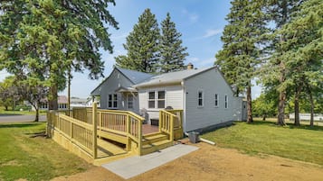 A single-story house with a covered porch and a small deck, surrounded by trees.