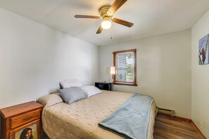 Ein Schlafzimmer mit einem Bett, einem Nachttisch, einer Lampe, einem Deckenventilator und einem Fenster mit Jalousien.