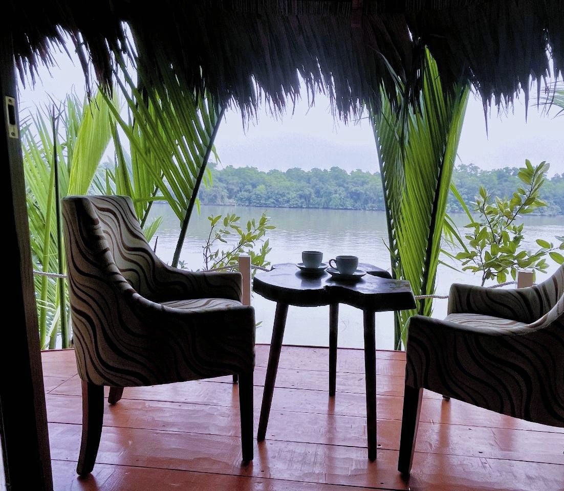 Un espace de repos abrité, avec deux chaises et une petite table, offrant une vue sur une étendue d’eau et une végétation luxuriante.