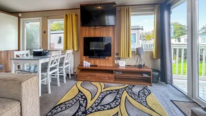 Quarto moderno com TV de tela plana, mobiliário de madeira, mesa de jantar e janelas amplas com vista para o exterior.