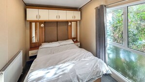 Quarto com cama, cabeceira de madeira, armários embutidos, janela com vista para o verde e radiador.