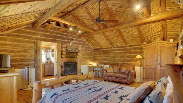 A log cabin interior with a bed, leather sofa, wooden dining table, and a fireplace. - Unwind Poolside, Scenic Sonoran Desert Retreat! (Tucson)
