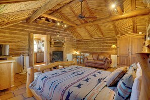 Ein rustikales Blockhaus-Interieur mit Bett, Ledersofa, Holzesstisch und Kamin.