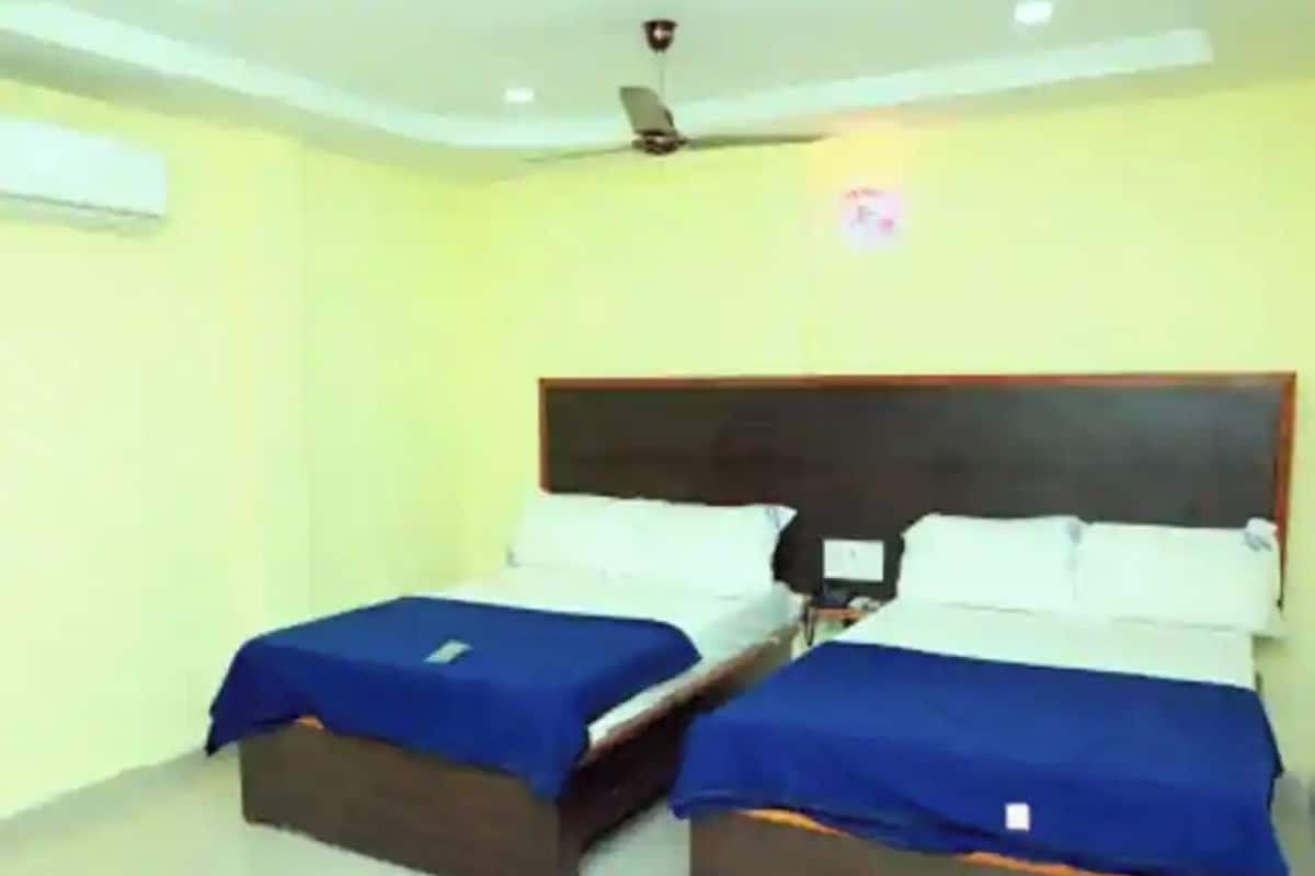 A room with two beds, each with a blue bedspread and white pillows, a wooden headboard, and a ceiling fan.