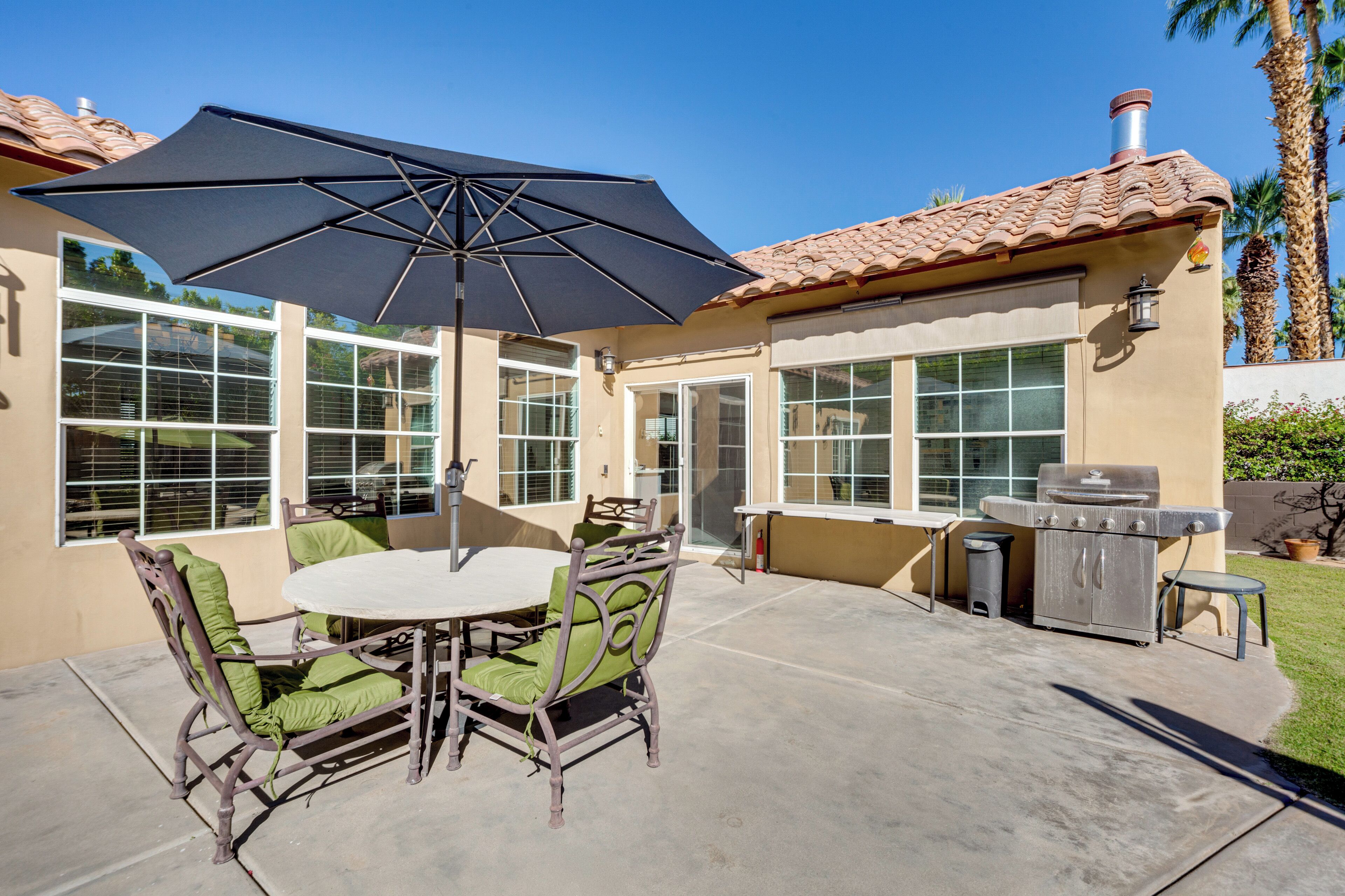 An outdoor patio with a table and chairs, a grill, and a large umbrella.