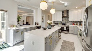 Une cuisine moderne dotée d’un grand îlot central, d’appareils électroménagers en acier inoxydable et de luminaires suspendus.