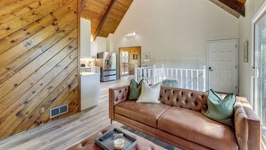 A spacious living area with a high ceiling, a leather sofa, and a wooden wall. - Deck + Views: Modern Cabin Near Lake Arrowhead! (Lake Arrowhead)