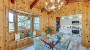 A wooden interior with a glass dining table, seating, and a kitchen area. - Deck + Views: Modern Cabin Near Lake Arrowhead! (Lake Arrowhead)