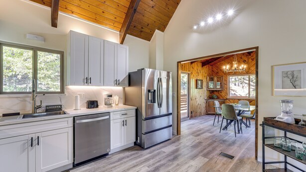 A modern kitchen with white cabinets, stainless steel appliances, and a wooden ceiling. - Deck + Views: Modern Cabin Near Lake Arrowhead! (Lake Arrowhead)