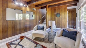 A spacious living room with wooden walls, a staircase, and two armchairs with cushions. - Deck + Views: Modern Cabin Near Lake Arrowhead! (Lake Arrowhead)