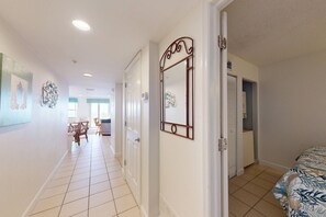 A hotel corridor with a dining area, a bed with a floral bedspread, and a wall-mounted mirror.