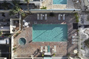 An aerial view of a hotel with a large rectangular pool, multiple lounge chairs, and a circular hot tub.