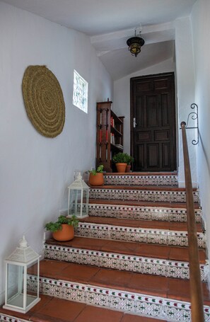 A staircase with patterned tiles, a wooden door, and potted plants. - Live an experience in a typical Andalusian house. (Almuñécar)