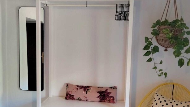 Un banco blanco con un cojín floral, una cesta colgante y un cojín de lunares.
