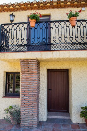 A building with a balcony, a door, and two potted plants. - Live an experience in a typical Andalusian house. (Almuñécar)