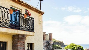 Un edificio con balcón, pilares de piedra y vista al mar.