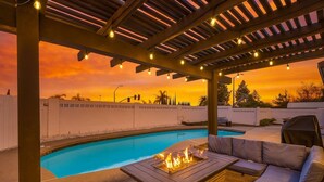 An outdoor pool area with a pergola, string lights, and a fire feature.