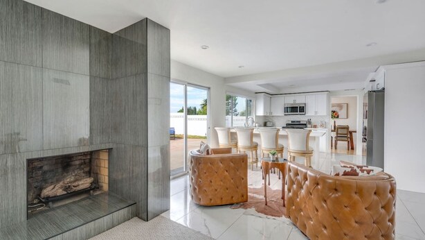 A modern living room with a fireplace, leather sofas, and a dining area with white chairs.