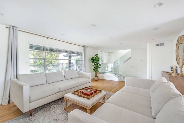 A spacious living room with a large window, a staircase, and a potted plant.