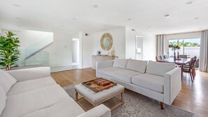 A spacious living room with a large white sofa, a wooden coffee table, and a dining area with a long table and chairs.