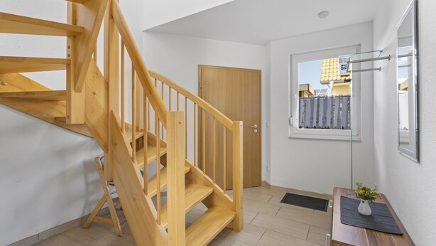 A modern interior with a wooden staircase, a door, a window with a view, and a small table with a vase. - Holiday home with sauna on the Baltic Sea (Boiensdorf)