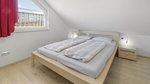 A bedroom with a sloped ceiling, a bed with striped bedding, a nightstand, a lamp, and a window with a red curtain. - Holiday home with sauna on the Baltic Sea (Boiensdorf)