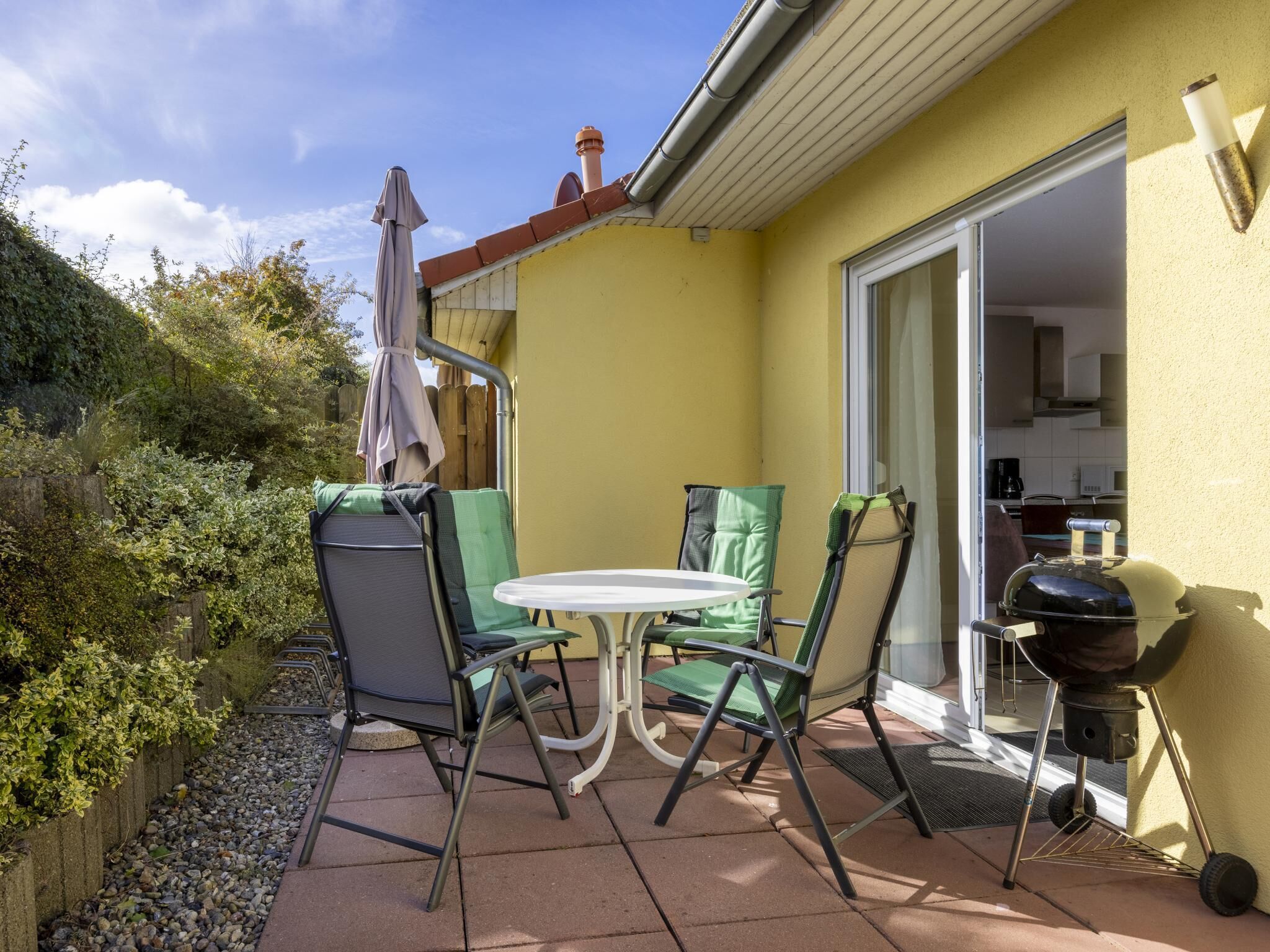 An outdoor patio with a table and chairs, a barbecue grill, and a door leading to a kitchen.