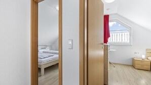 Une chambre à coucher avec un lit, une fenêtre ornée d’un rideau rouge, une table de chevet et une armoire en bois.