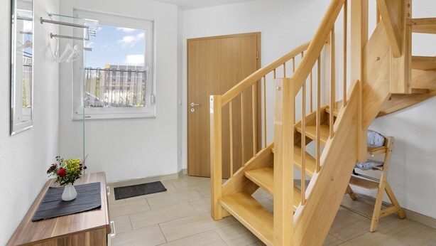 Un appartement moderne avec un escalier en bois, une petite table ornée d’un vase de fleurs et une fenêtre donnant sur des immeubles.