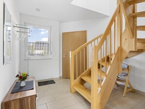 Een modern appartement met een houten trap, een klein tafeltje met een bloemenvaas, en een raam met uitzicht op gebouwen.