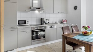 Une cuisine moderne avec des meubles gris, un four encastré, un micro-ondes, une machine à café et un grille-pain. On y trouve une table à manger avec des chaises et un vase de fleurs.