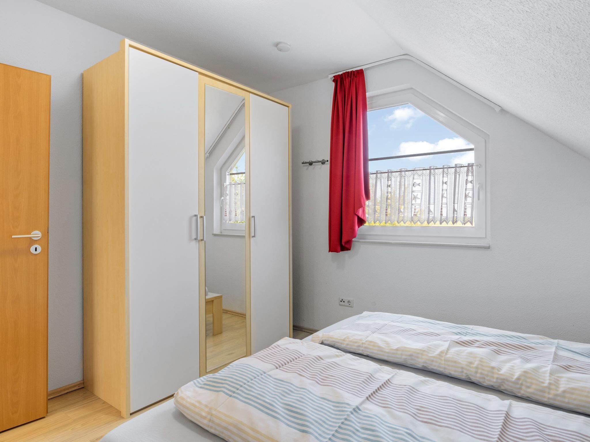 A bedroom with a bed, a wardrobe, a window with a view, and a red curtain.